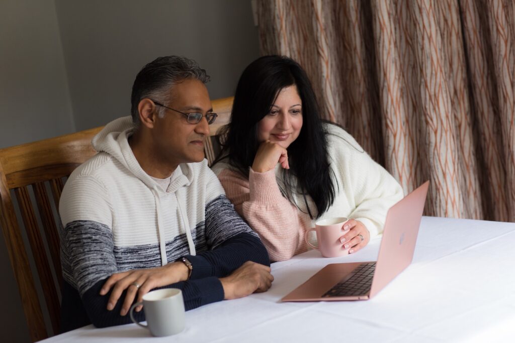 two adults looking at laptop drinking a hot drink