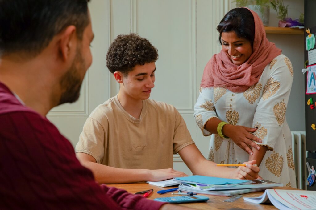 teenager doing work at dining table with two adults looking on