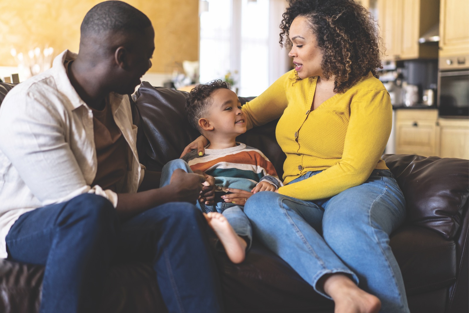 Two adults with pre school age child reading a book on a sofa